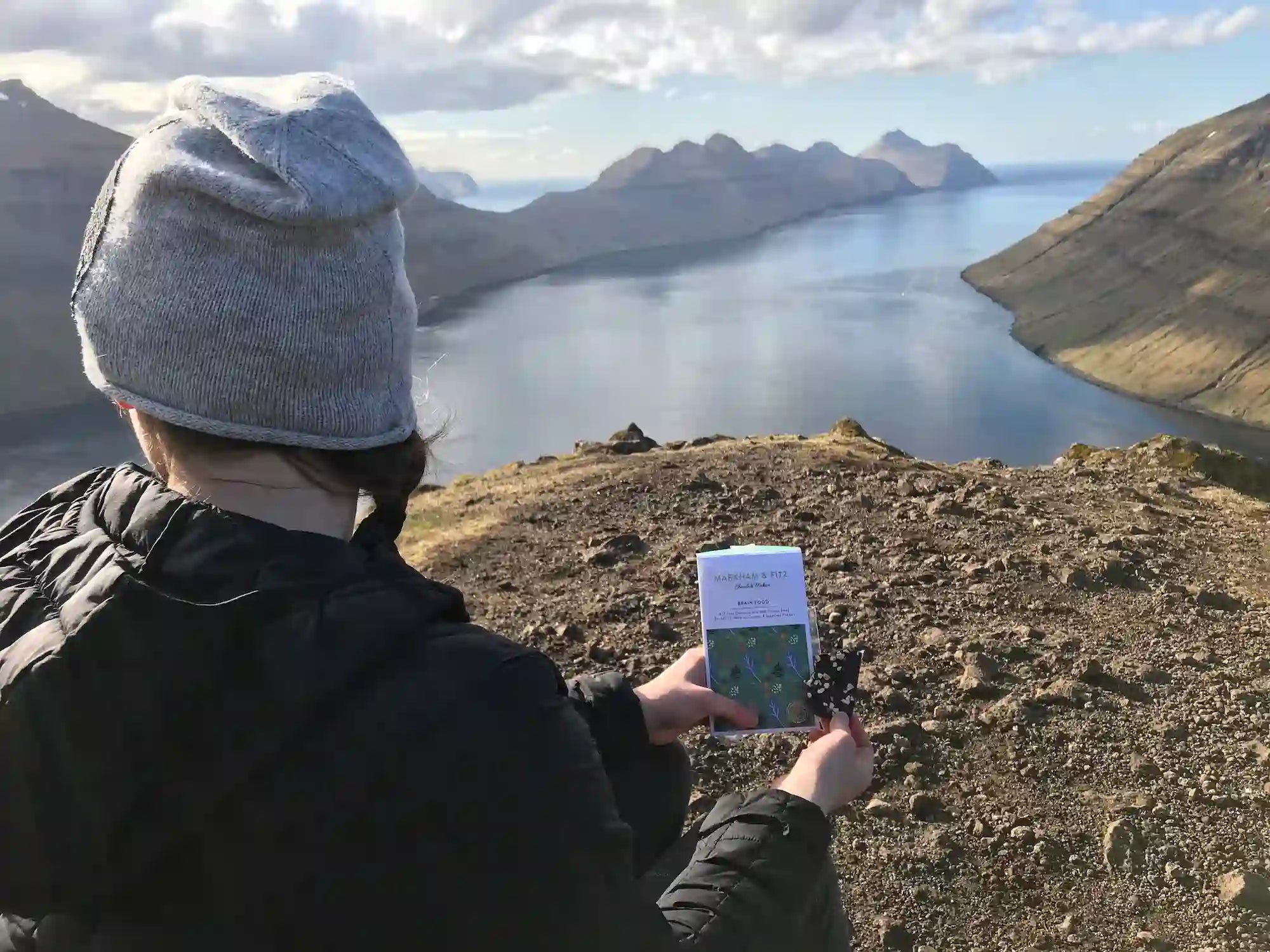 Lauren holding Brain Food with a background of calm water and distant mountains.