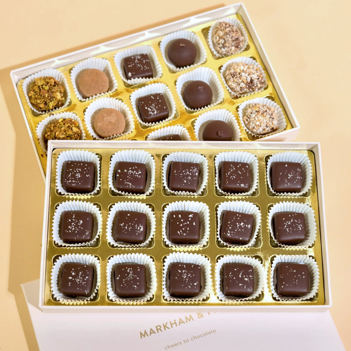 Two open Markham & Fitz boxes of 15 sea salt caramels and truffles stacked on a peach background