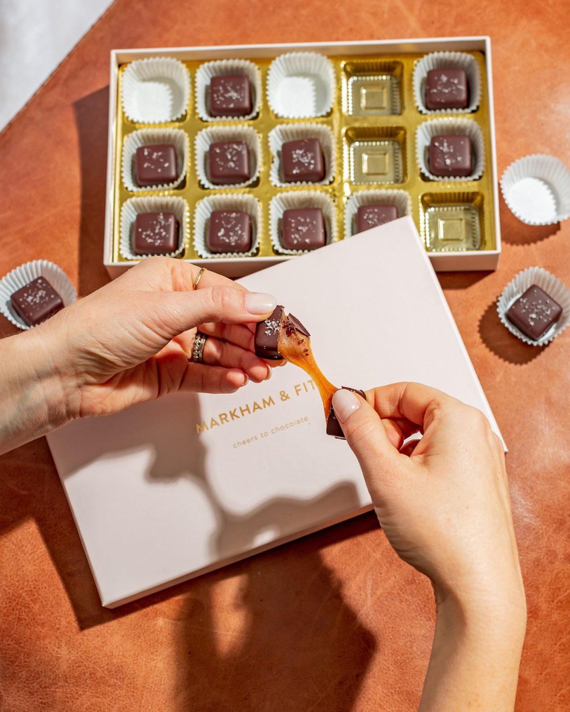 Hands pulling apart a sea salt caramel, showing the caramel stretch