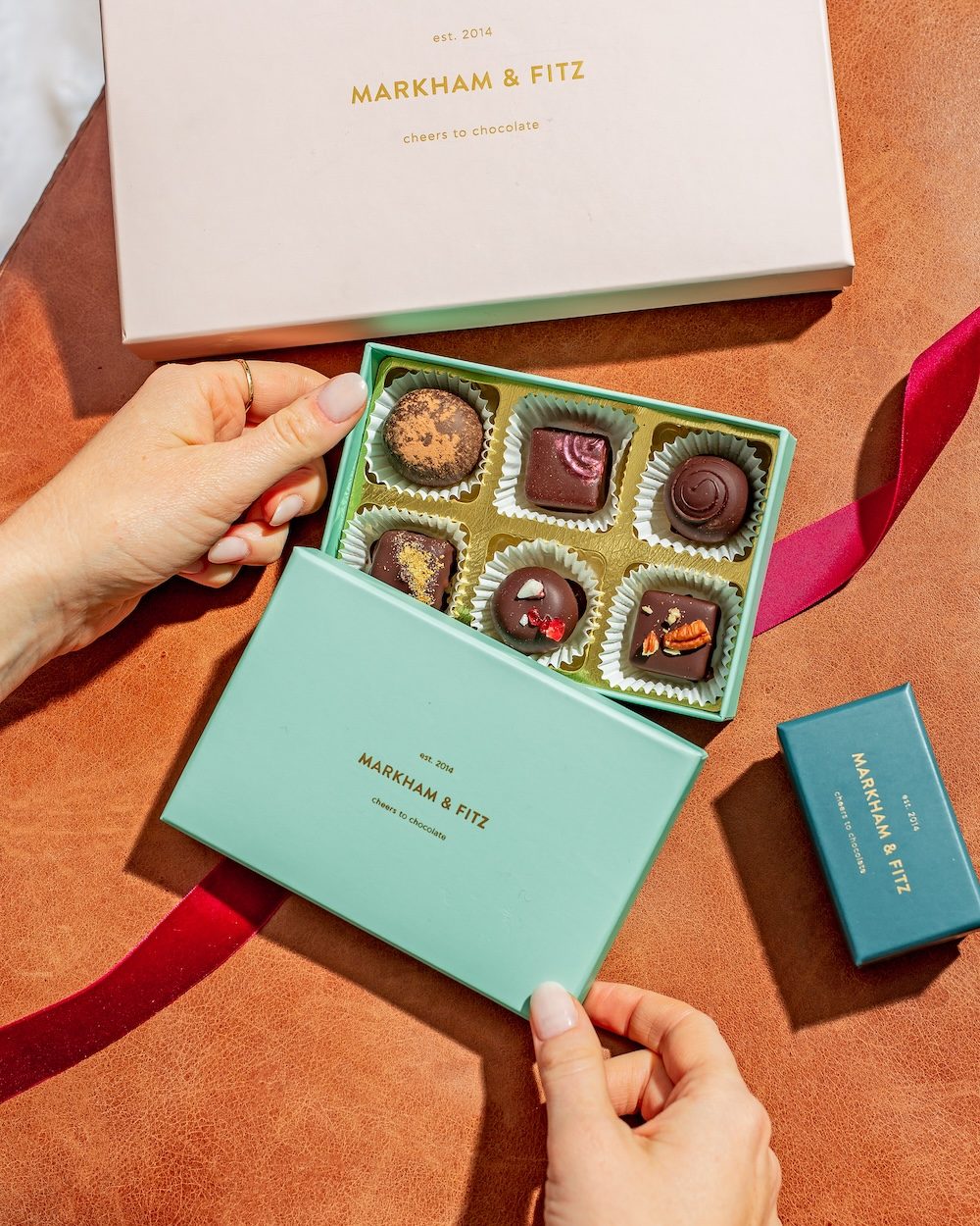 Hands opening a mint box of six truffles beside a pink gift box