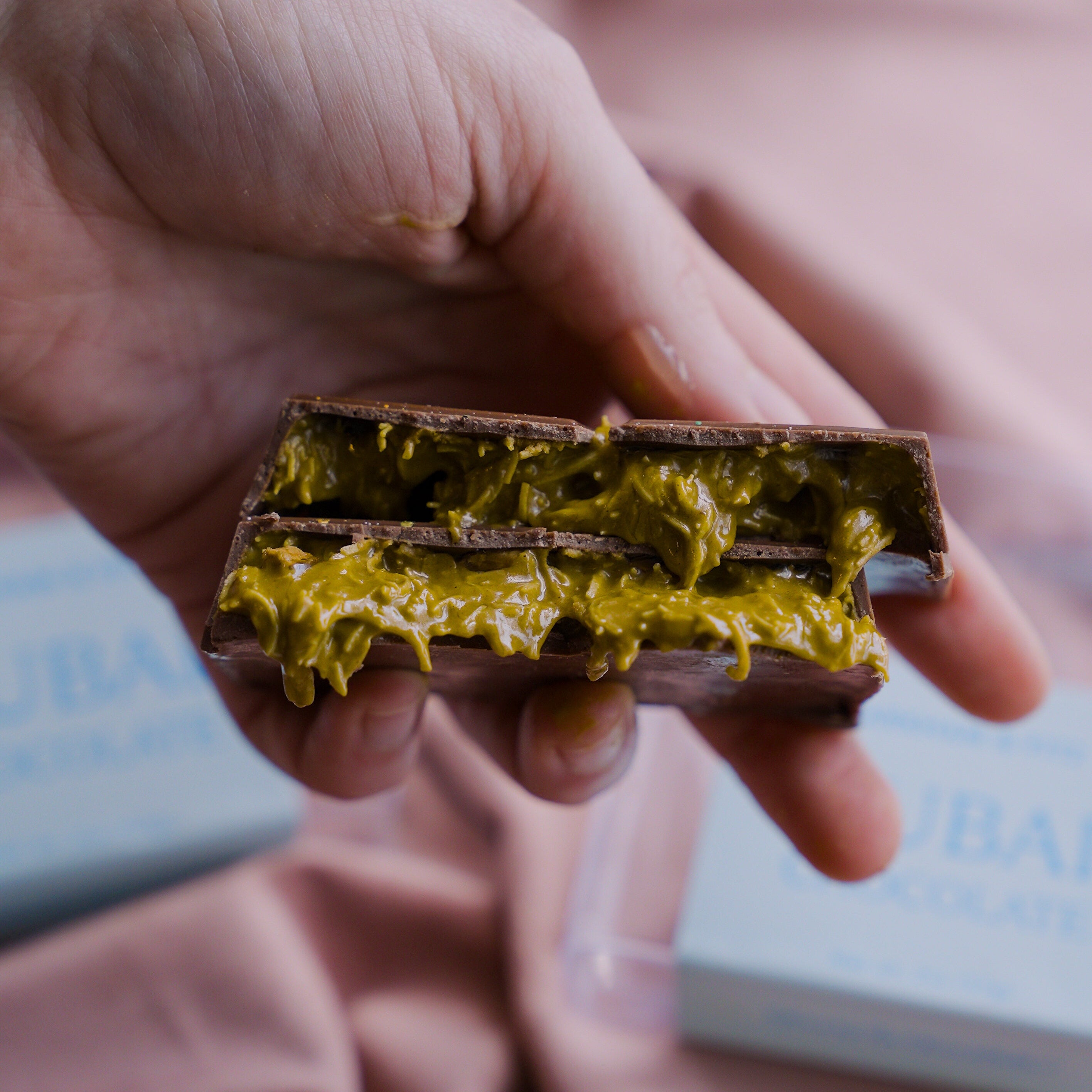 Hand holding a chocolate bar with a yellow filling against a pink fabric background