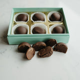 Box of chocolate truffles with some outside the box on a light surface